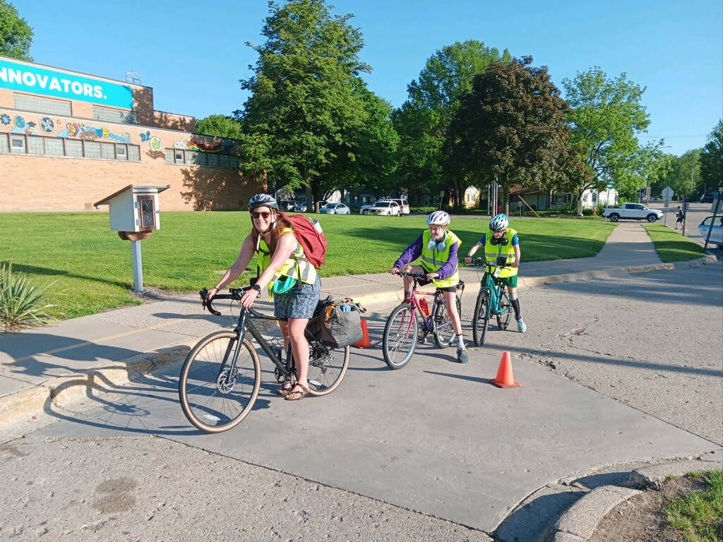 A C-U SRTS volunteer leads two students towards a school on their bicycles.